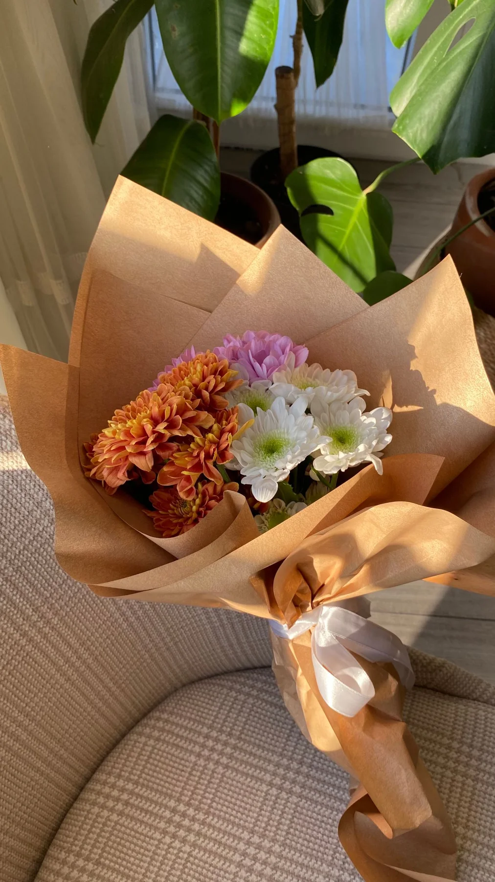 A bouquet of flowers wrapped in brown paper resting on a chair.
