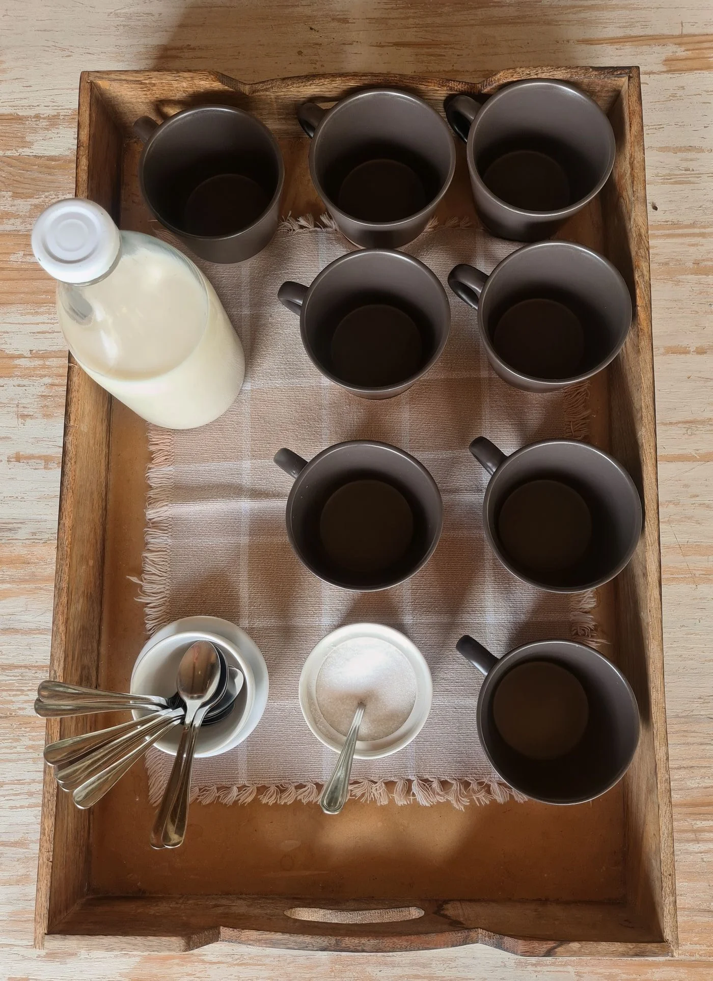 A wooden tray holding mugs, milk, sugar, and spoons.