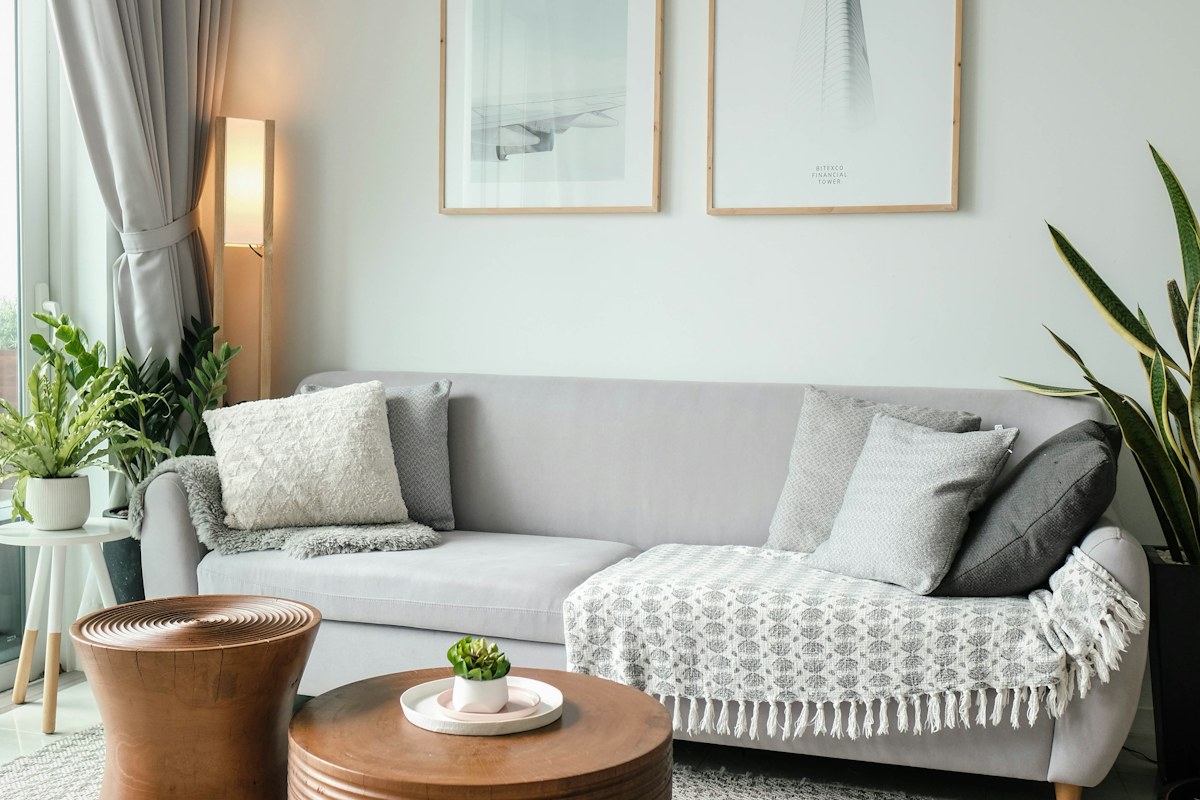 A pale sofa with cushions beside large windows and a small round table