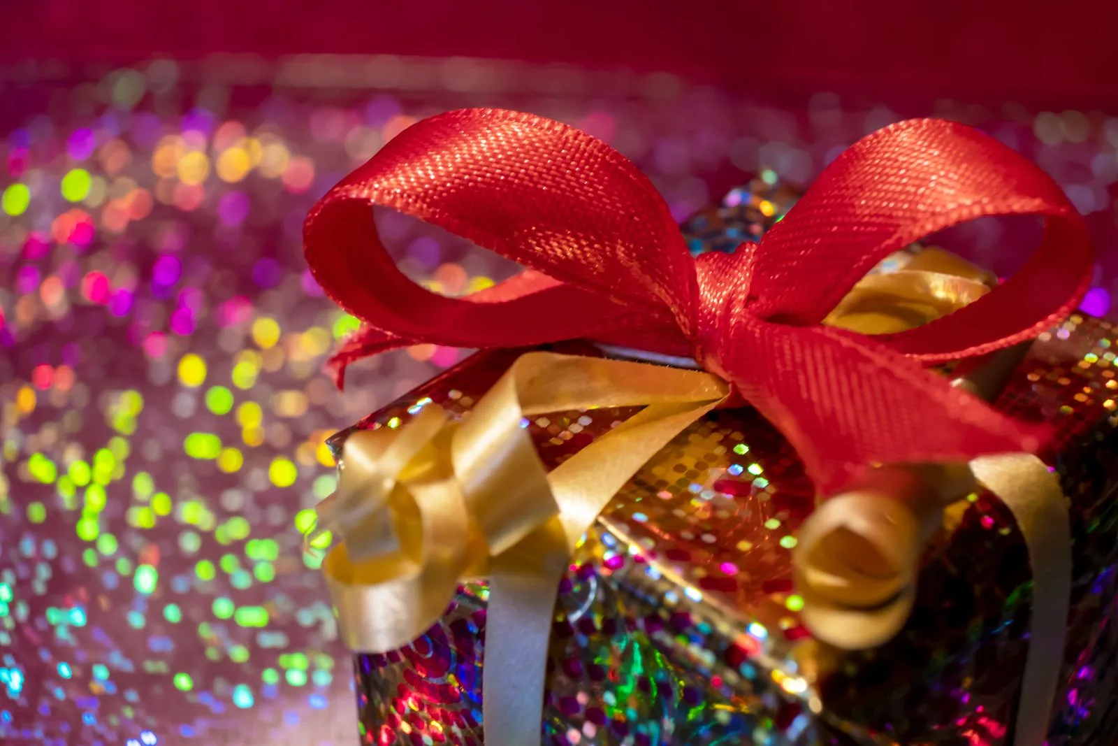 A red and gold ribbon bow on sparkling gift wrapping