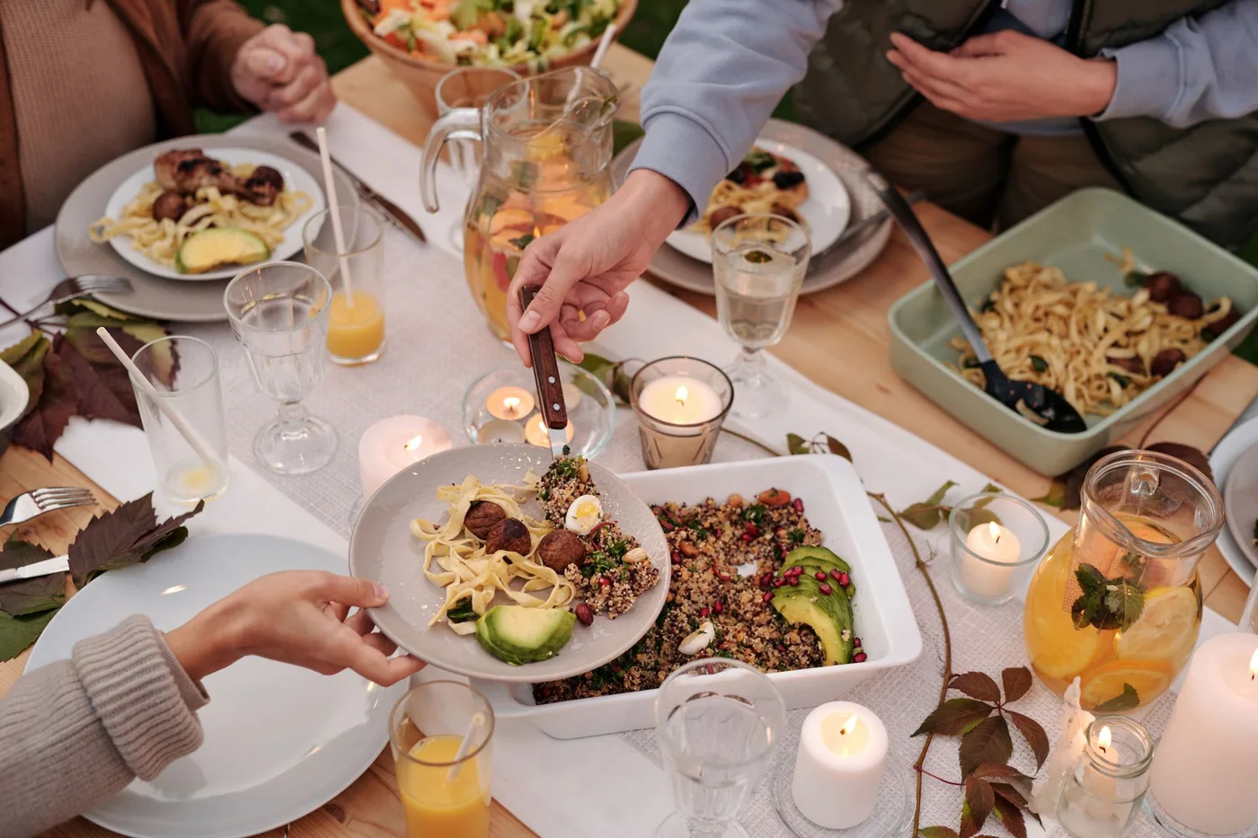 People sharing plated food and drinks around a table with lit candles