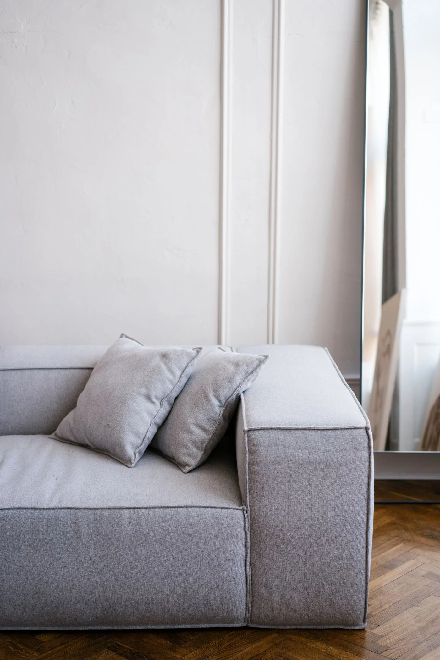 A gray sofa beside a large mirror in a bright room.