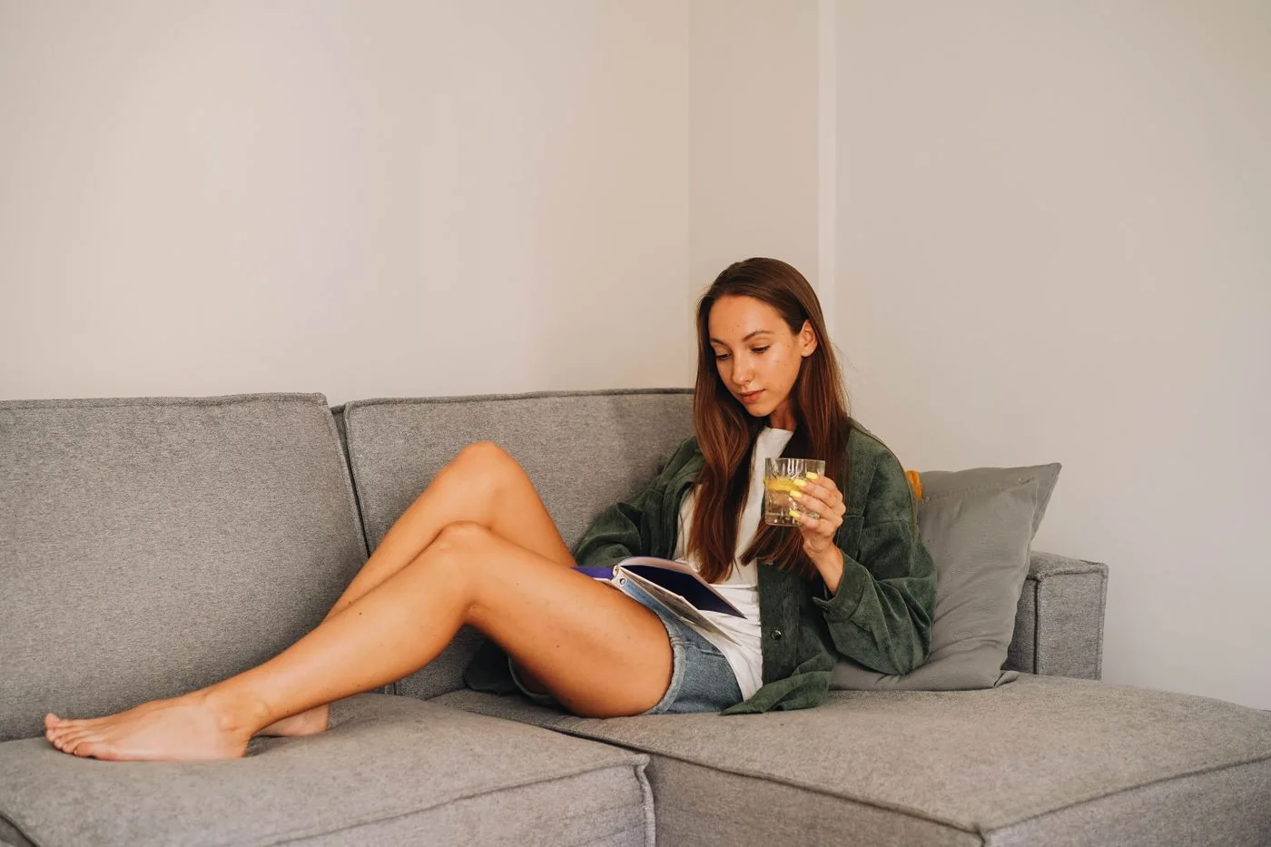 A person reading a book on a gray sofa.