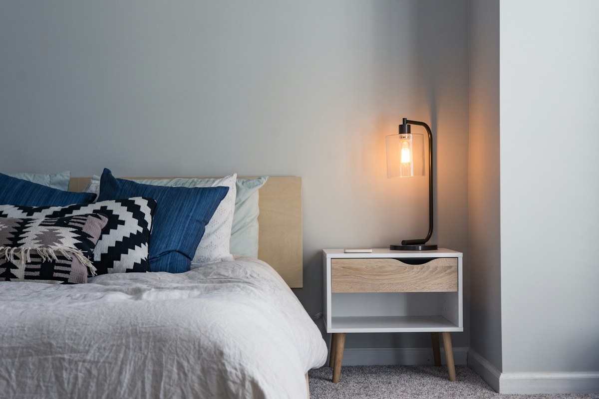A bedside table and lit lamp beside a bed.