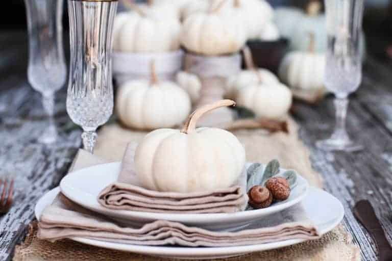 Beautiful fall tablescape with white dishes, pumpkins, and natural color napkins