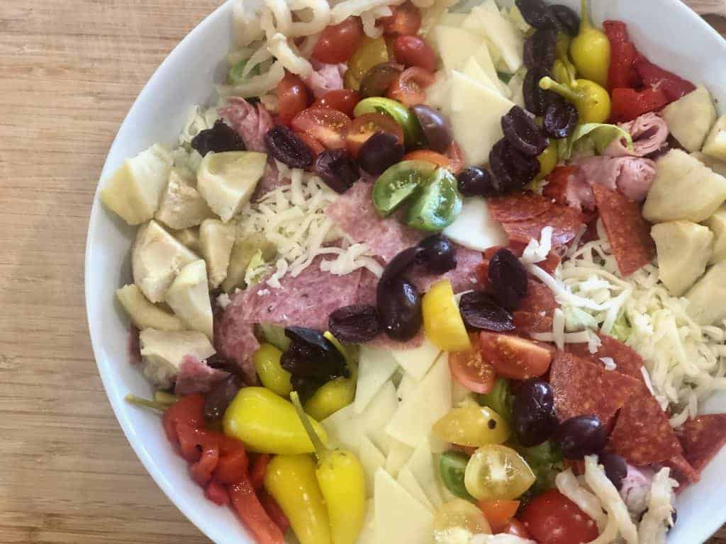 A photo of a antipasto salad with cured meats, cheese, artichoke hearts, olives, and tomatoes