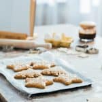 A counter with a cookie tray, surrounded by baking essentials like a rolling pin and vanilla. Star shaped cookies on silver try.