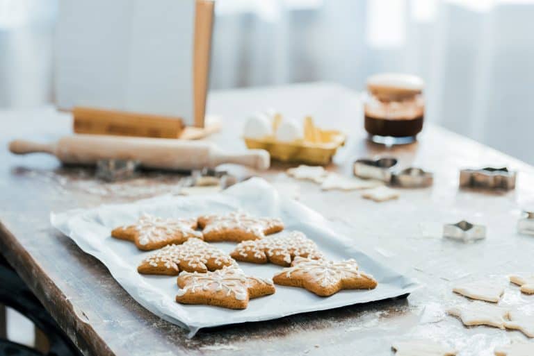 A counter with a cookie tray, surrounded by baking essentials like a rolling pin and vanilla. Star shaped cookies on silver try.