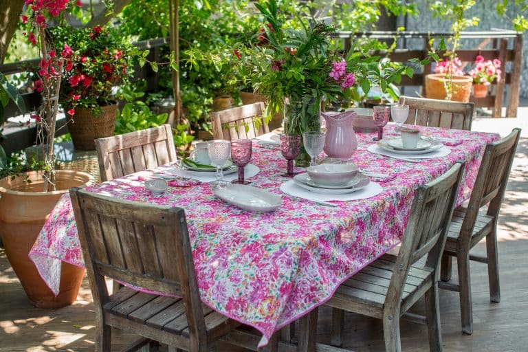 Lunch table with empty dish set on colorful tablecloth in pink and bouquet of freshly picked garden flowers set outside.