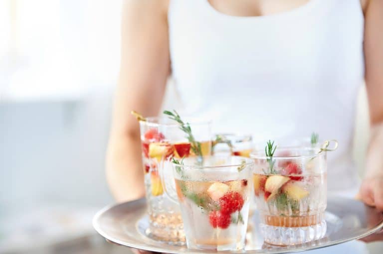 woman in white tank holding a silver tray with short glasses that have mocktails in them.