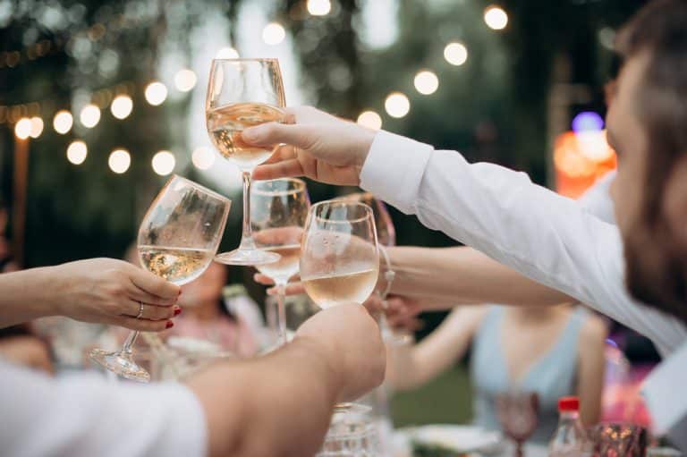 A cocktail reception for a wedding with the bride and groom and guests toasting with white lights in the background