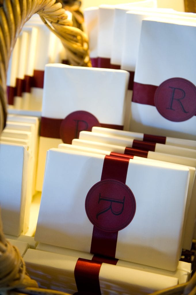 Books wrapped in white paper with burgundy ribbon and an initial R set in a basket used as favors for a wedding.
